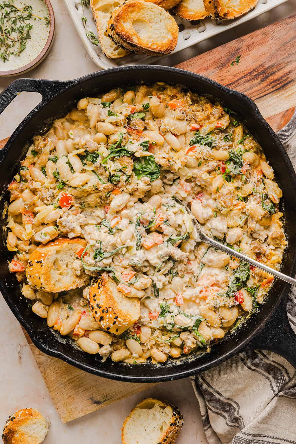 This Cheesy Sausage Bean Dip is the ultimate party appetizer! Made with flavorful spicy sausage, sautéed onions, bell peppers, garlic and spinach, along with cream cheese and white beans. Topped with freshly grated parmesan cheese and served with toasted bread or Frito corn chips!
