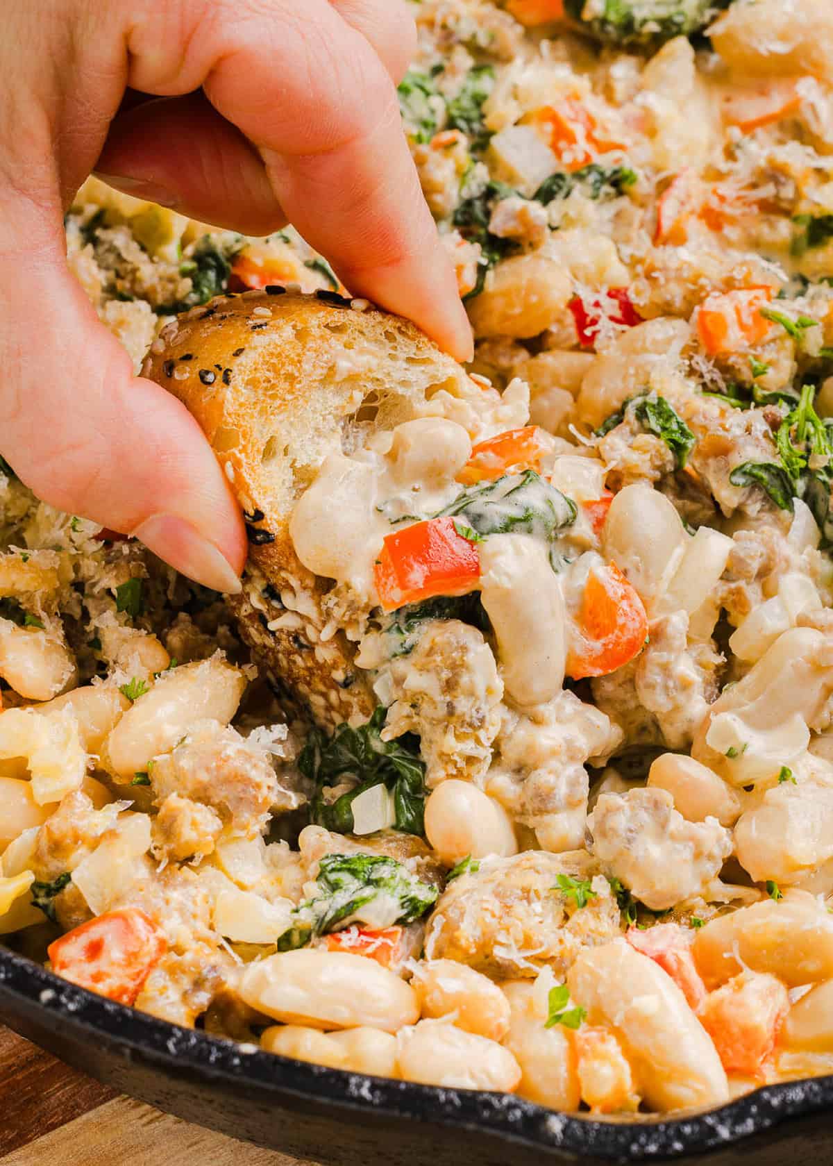 This Cheesy Sausage Bean Dip is the ultimate party appetizer! Made with flavorful spicy sausage, sautéed onions, bell peppers, garlic and spinach, along with cream cheese and white beans. Topped with freshly grated parmesan cheese and served with toasted bread or Frito corn chips!