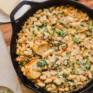 This Cheesy Sausage Bean Dip is the ultimate party appetizer! Made with flavorful spicy sausage, sautéed onions, bell peppers, garlic and spinach, along with cream cheese and white beans. Topped with freshly grated parmesan cheese and served with toasted bread or Frito corn chips!