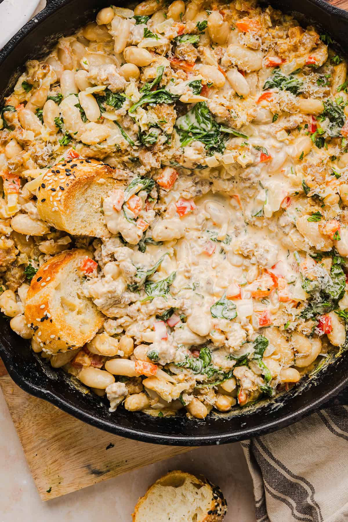 This Cheesy Sausage Bean Dip is the ultimate party appetizer! Made with flavorful spicy sausage, sautéed onions, bell peppers, garlic and spinach, along with cream cheese and white beans. Topped with freshly grated parmesan cheese and served with toasted bread or Frito corn chips!